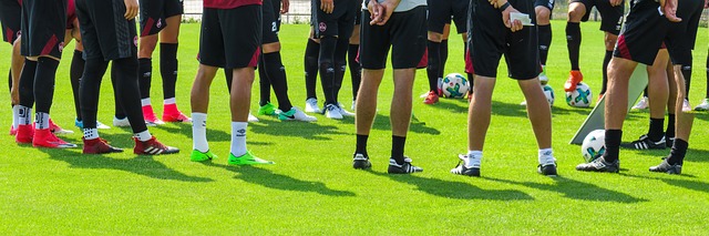 Football players standing in a circle next to footballs on the grass with a coach and tactics board