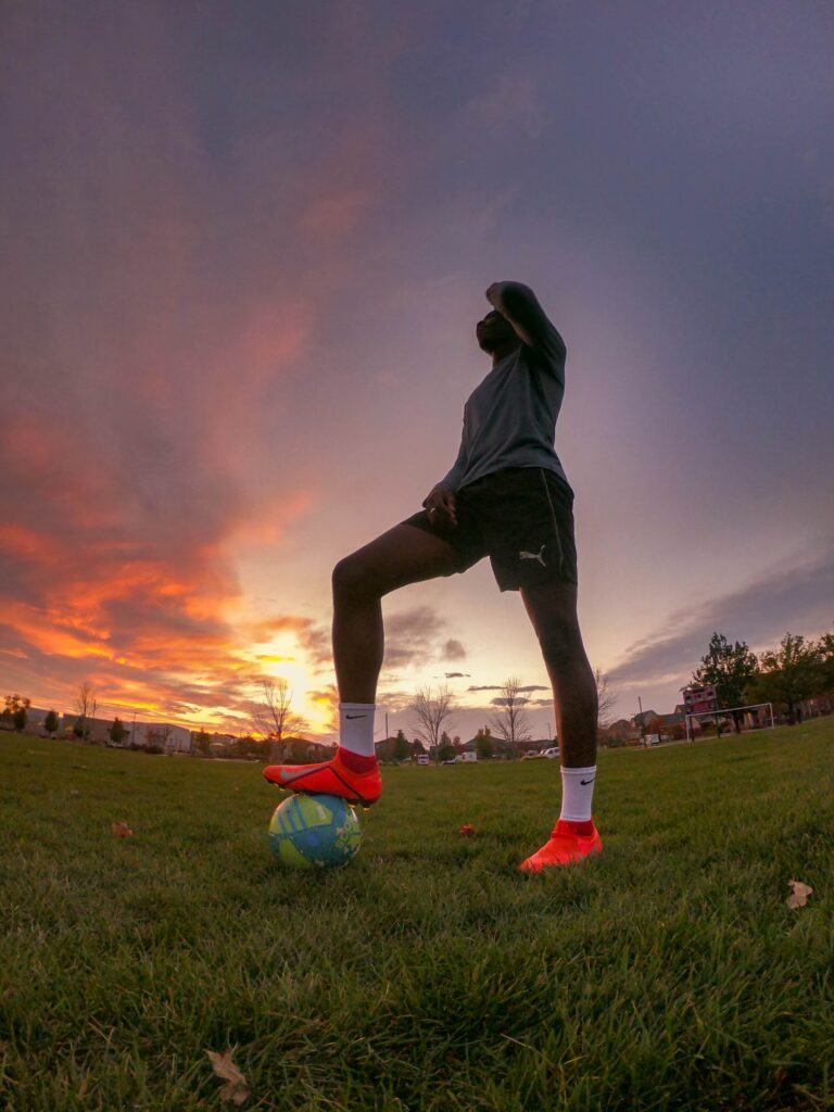 Football player with his foot on the ball in a field at sunset
